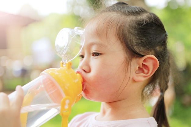 Ciérrese encima del agua potable de la botella de la niña pequeña en el parque.