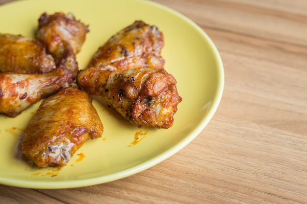 Ciérrese encima de las alas de pollo frito en plato verde en la tabla de madera