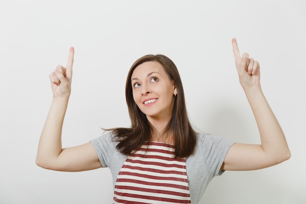 Ciérrese encima de ama de casa caucásica morena sonriente atractiva joven en delantal aislado. Hermosa mujer ama de llaves apuntando con el dedo índice hacia arriba mirando hacia arriba