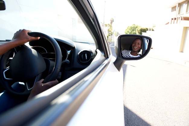 Ciérrese encima del coche que conduce negro sonriente y que mira en el espejo lateral