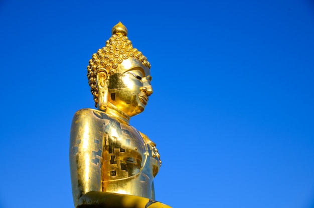 Ciérrese encima de la estatua de oro vieja de Buda contra con el cielo azul