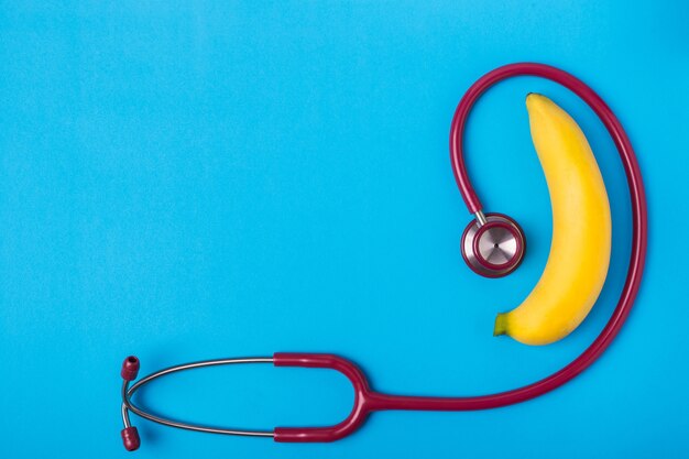 Ciérrese encima del estetoscopio y del plátano amarillo en fondo azul