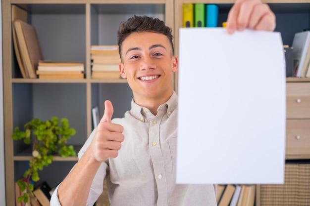 Ciérrese encima del foco en el hombre que sostiene la hoja en blanco para copiar el espacio. Empleado masculino caucásico joven atractivo sonriente que recomienda buen servicio, satisfecho con la carrera exitosa en la empresa internacional.