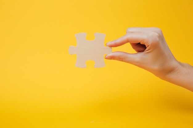 Ciérrese encima de la foto recortada de la mano que sostiene la pieza del rompecabezas de madera aislada en el fondo amarillo brillante de la pared. Concepto de asociación y conexión. Copie el espacio publicitario de maquetas.