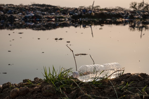 Foto ciérrese encima de una gota plástica clara de la botella en el suelo con agua contaminada y basura grande de la montaña en el fondo