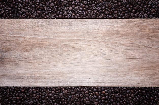 Ciérrese encima de los granos de café en el fondo de madera, composición con el espacio libre de la madera