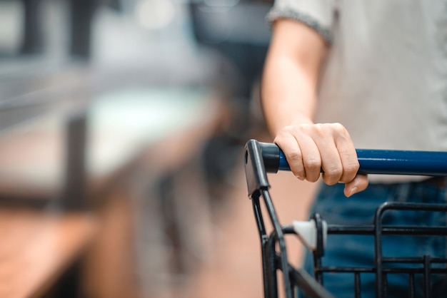 Ciérrese encima de la mano del comprador femenino con la carretilla, carro de compras en el supermercado.