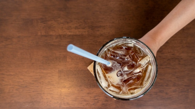 Ciérrese encima de la mano de la mujer que sostiene el café solo del hielo en cafetería