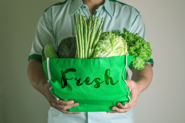 Ciérrese encima de la mano que sostiene la bolsa de supermercado verde de las verduras verdes orgánicas mezcladas, compras orgánicas sanas de la comida verde y terapia de la nutrición de la atención sanitaria de la dieta