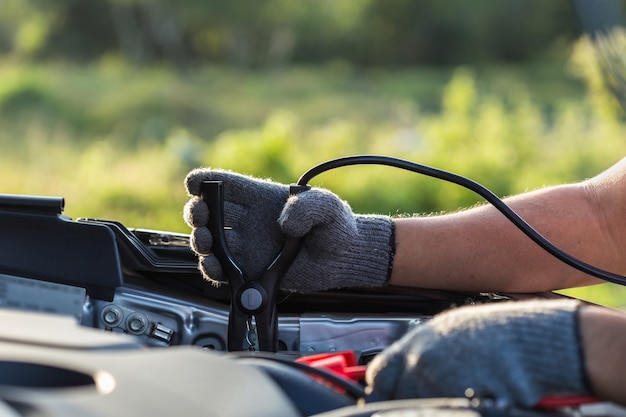 Ciérrese encima de la mano del técnico del coche que sostiene el cable para conectar con la batería