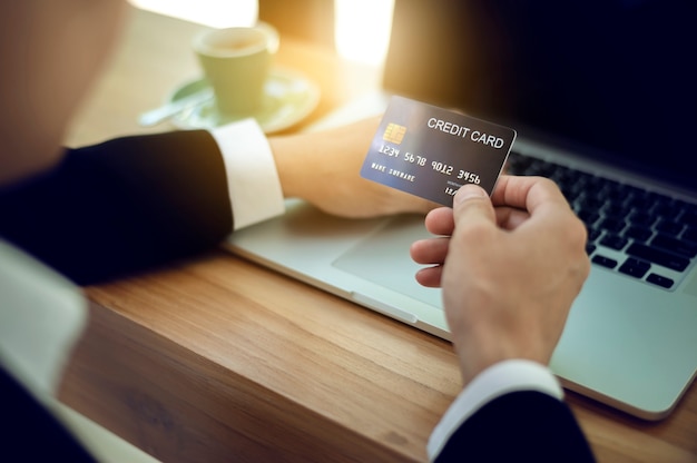 Foto ciérrese encima de las manos del hombre de negocios que sostienen la tarjeta de crédito y que usan el labtop que hace el pago en línea. concepto de compra en línea.