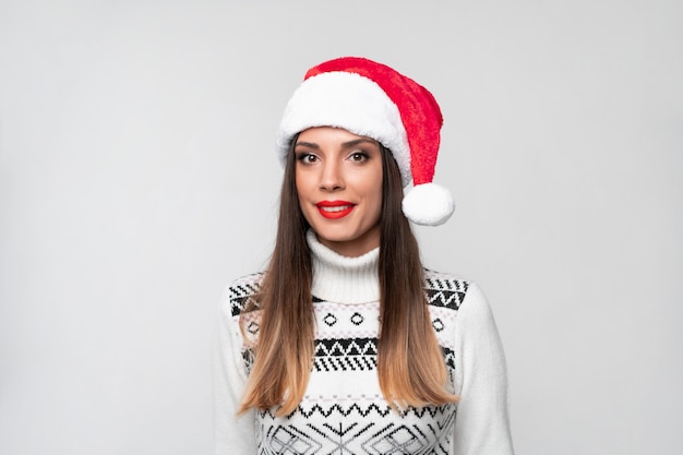 Ciérrese encima de la mujer caucásica beautifiul del retrato en el sombrero rojo de Papá Noel en la pared blanca. Concepto de Navidad año nuevo. Linda mujer dientes sonriendo emociones positivas con espacio de copia libre