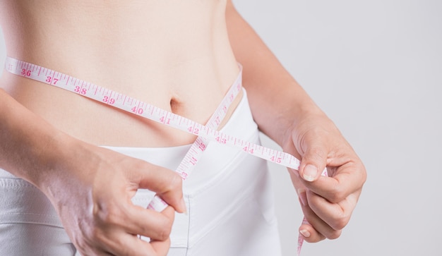 Ciérrese encima de la mujer delgada que mide su cintura delgada. Concepto de estilo de vida de la dieta de la salud y la mujer para reducir el vientre y dar forma al músculo del estómago sano.