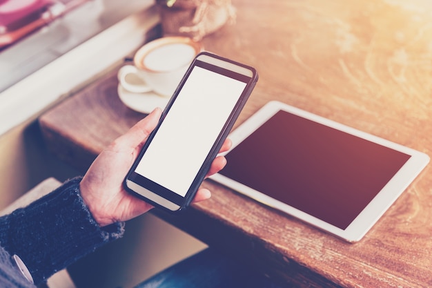 Ciérrese encima de la mujer de la mano que usa el teléfono en cafetería con tono del vintage.