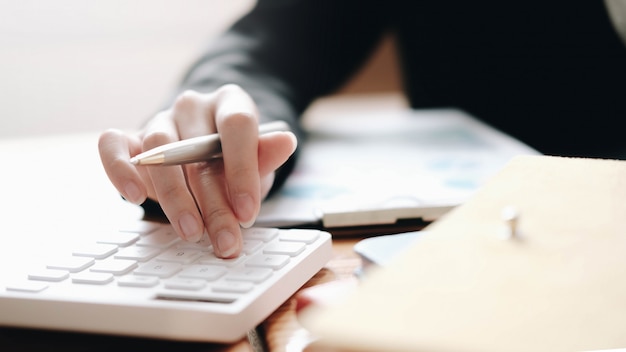 Ciérrese encima de la mujer de negocios que usa la calculadora y la computadora portátil para las finanzas de las matemáticas en el escritorio de madera