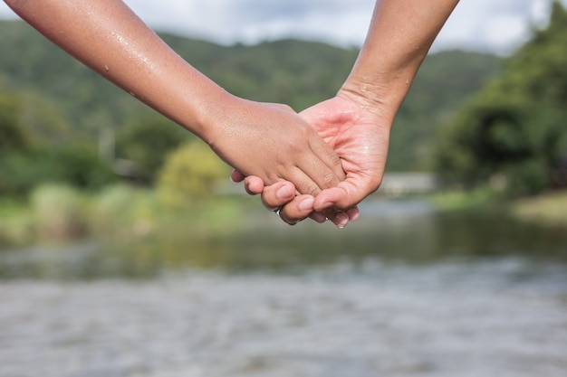 Ciérrese encima de la mujer que lleva a cabo su mano de la hija en el río. Concepto de ayuda