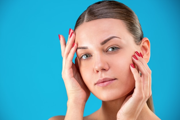 Foto ciérrese encima del retrato de la belleza de la morenita de la mujer joven que sonríe y que toca su cara en la pared azul. piel fresca y perfecta. concepto de juventud y cuidado de la piel.