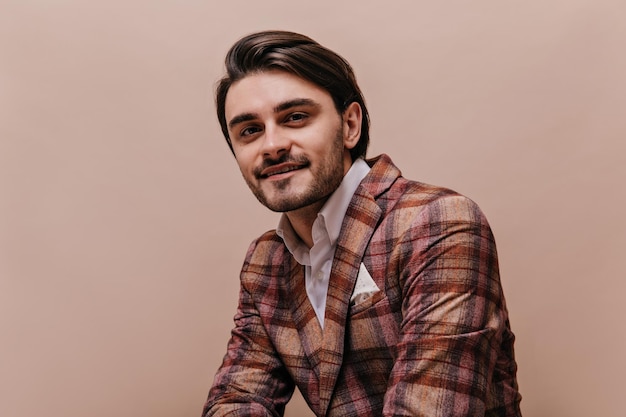 Ciérrese encima del retrato del caballero joven lindo en la chaqueta a cuadros retro y la camisa blanca que mira directamente y que sonríe contra fondo beige