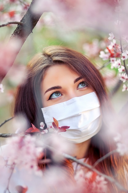 Foto ciérrese encima del retrato de la chica joven debajo de un albaricoquero floreciente con una máscara del coronavirus.