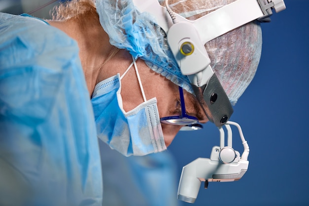 Foto ciérrese encima del retrato de la doctora cirujana que lleva la máscara protectora y el sombrero durante la operación