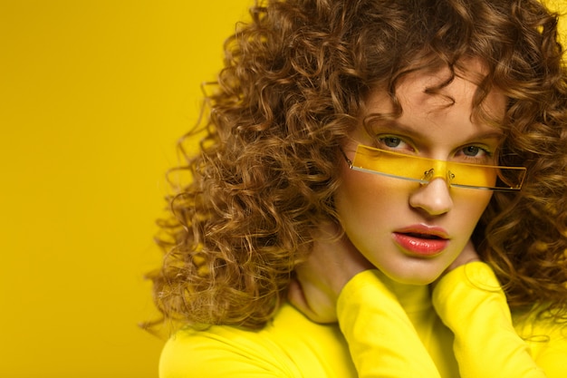 Ciérrese encima del retrato del estudio de la moda de mujeres hermosas jovenes con el pelo rizado