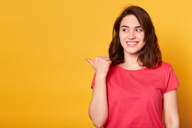 Ciérrese encima del retrato de la hembra joven bien vestida del pelo de Gark en ropa casual que señala a la izquierda con el pulgar y que mira a un lado con la expresión feliz y la sonrisa dentuda