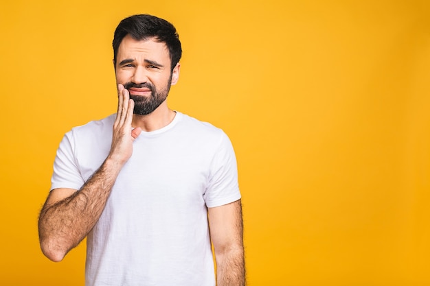 Ciérrese encima del retrato del hombre barbudo apuesto preocupado infeliz nervioso que toca su mejilla que tiene dolor de muelas aislado en el copyspace del fondo amarillo.