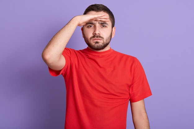 Ciérrese encima del retrato del hombre barbudo hermoso serio que mira en la distancia, sosteniendo la mano en la frente, posando aislada contra la pared púrpura