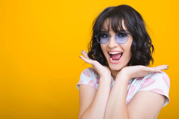 Ciérrese encima del retrato de la morena joven linda que grita asombrada mientras mira la cámara delante de una pared amarilla.