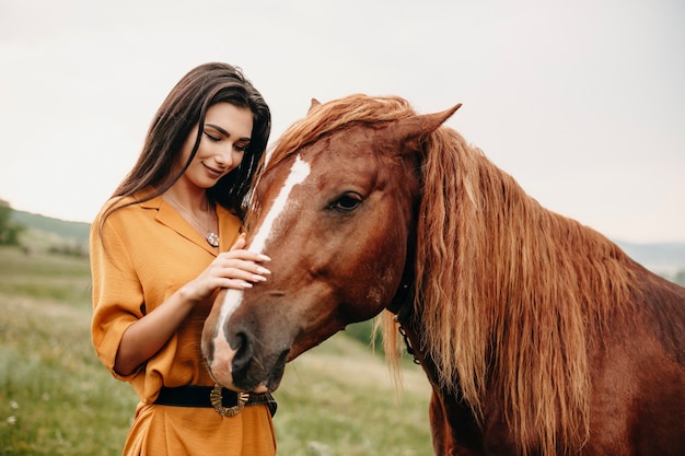 Ciérrese encima del retrato de una muchacha encantadora joven que abraza un caballo en un campo. Joven mujer caucásica sonriendo tocando un caballo mientras viaja.