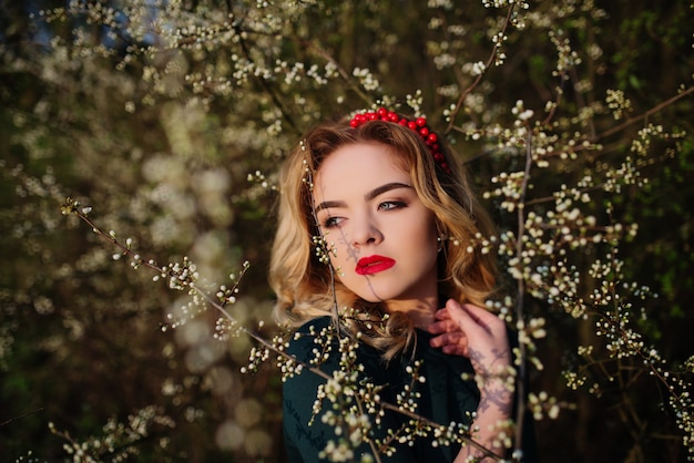 Ciérrese encima del retrato de la muchacha rubia elegante de Yong en el vestido verde en el jardín en primavera en árboles del flor.