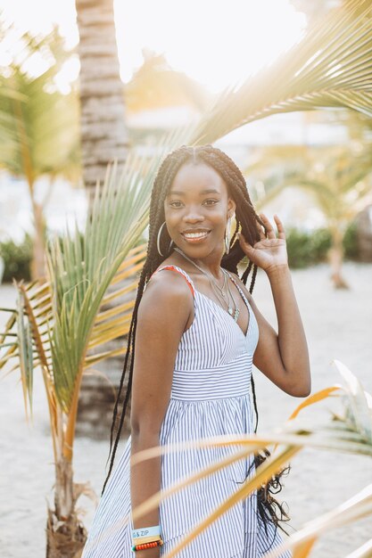 Ciérrese encima del retrato de la mujer africana joven hermosa cerca de la palma en la playa