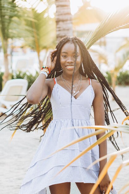 Ciérrese encima del retrato de la mujer africana joven hermosa cerca de la palma en la playa