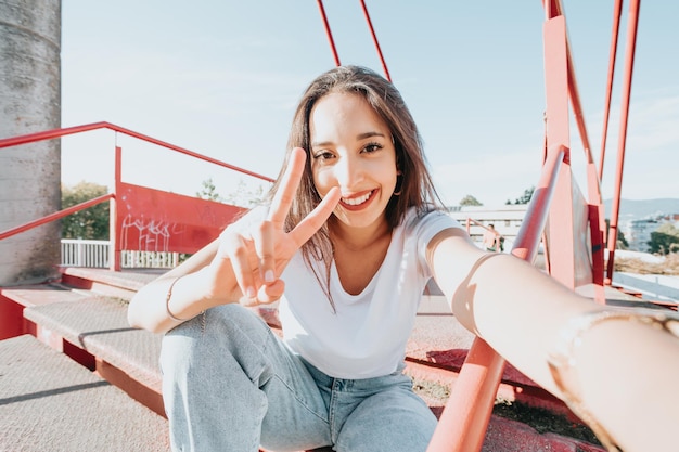 Ciérrese encima del retrato de la mujer árabe joven que mira lejos de la camisa blanca de la cámara y de los pantalones vaqueros azules en la calle. Engreimiento. Estilo de vida en la calle, moda fresca. Concepto de red social. Disparo de gran angular