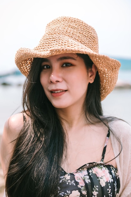 Ciérrese encima del retrato de la mujer asiática hermosa que lleva la emoción feliz del sombrero en la playa en verano en vacaciones