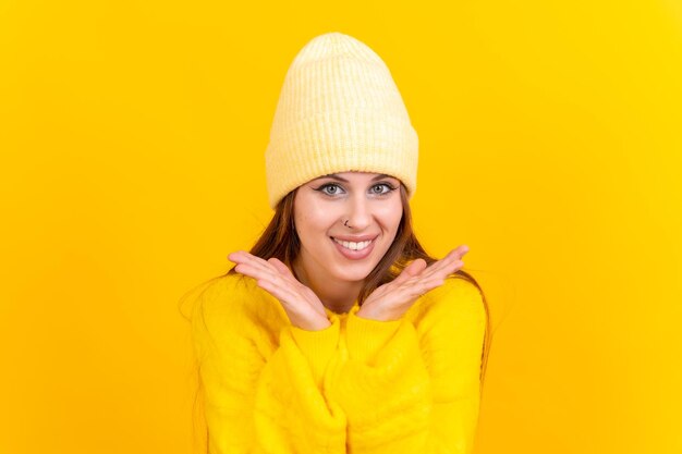 Ciérrese encima del retrato de la mujer joven alegre aislada en el fondo amarillo del estudio en suéter de lana amarillo