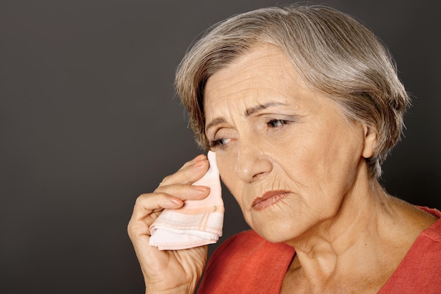 Ciérrese encima del retrato de la mujer mayor hermosa que llora aislada en fondo gris