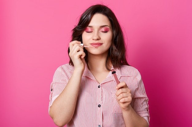 Ciérrese encima del retrato de la mujer morena hermosa que sostiene y que huele brillo labial dulce