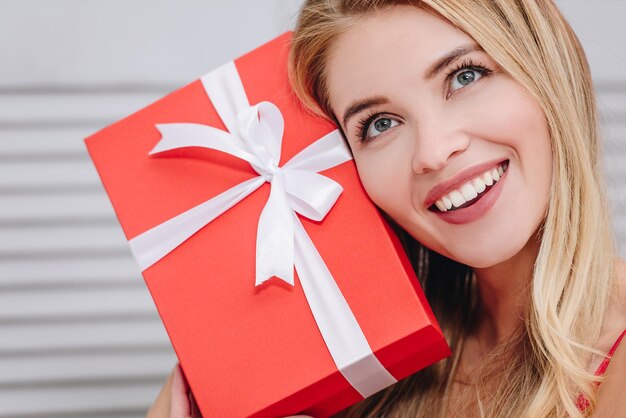 Ciérrese encima del retrato de la mujer sonriente que sostiene la caja de regalo en el concepto del día de san valentín de la cara