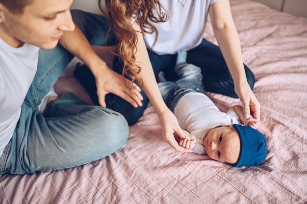 Ciérrese encima del retrato de los padres felices que detienen a su bebé. Joven familia feliz, mamá y papá jugando con lindo emocional pequeño hijo recién nacido en el dormitorio