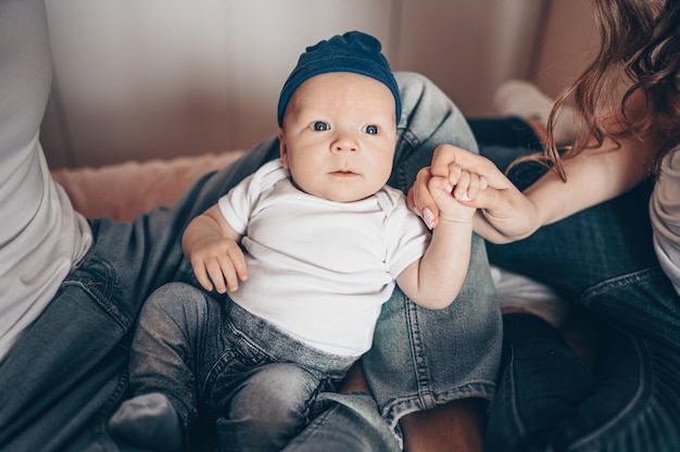 Ciérrese encima del retrato de los padres felices que detienen a su bebé. Joven familia feliz, mamá y papá jugando con lindo emocional pequeño hijo recién nacido en el dormitorio