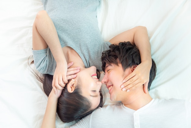 Ciérrese encima del retrato de la pareja asiática bastante joven con felicidad. Asia el hombre y la mujer yacían en la cama mirando juntos con una gran sonrisa mano toque la cara, amor emoción con concepto de San Valentín