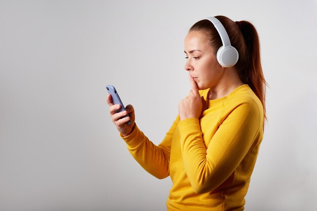 Ciérrese encima del retrato del podcast femenino caucásico o de la música que escucha en fondo gris. escuchando musica en auriculares