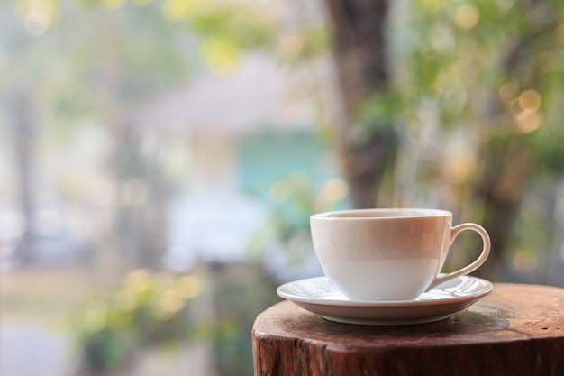 Ciérrese encima de la taza del café con leche en la tabla en jardín con el bokeh ligero de la falta de definición