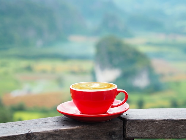 Ciérrese encima de la taza roja de café con leche sobre la montaña borrosa