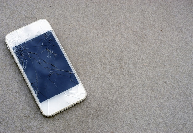 Ciérrese encima del teléfono móvil moderno con la pantalla quebrada en la carretera de asfalto