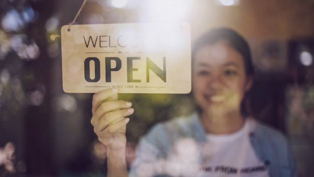 Ciérrese encima del tiro de la mano de la mujer que da vuelta al tablero abierto de la muestra en la puerta de cristal en cafetería.