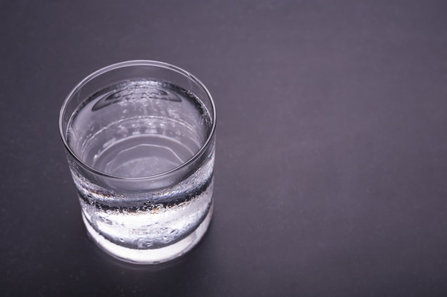 Ciérrese encima del vidrio de agua fría en fondo negro de la tabla