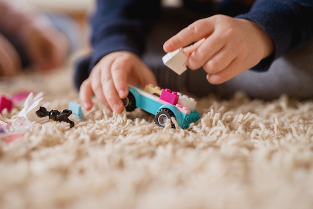 Foto ciérrese encima de la vista del foco del coche plástico del juguete de bloques mientras que las manos del niño pequeño hacen una nueva forma.