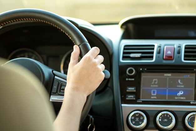 Ciérrese encima de la vista de las manos de la mujer que sostienen el volante que conduce un coche en la calle de la ciudad el día soleado.